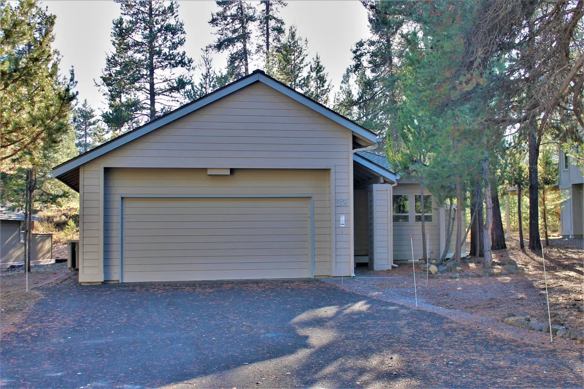 An inviting front entrance and garage door framed by mature trees, offering a welcoming view of the home's exterior as guests arrive. The scene hints at privacy, comfort, and the seamless blend of home and nature.