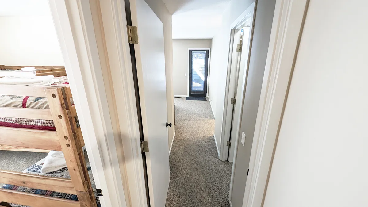 This interior image shows cozy bunk beds with a doorway leading outside and a carpeted hallway, suggesting both indoor fun and easy access to outdoor adventures. Natural light filters in, making the space playful and inviting for families with children.
