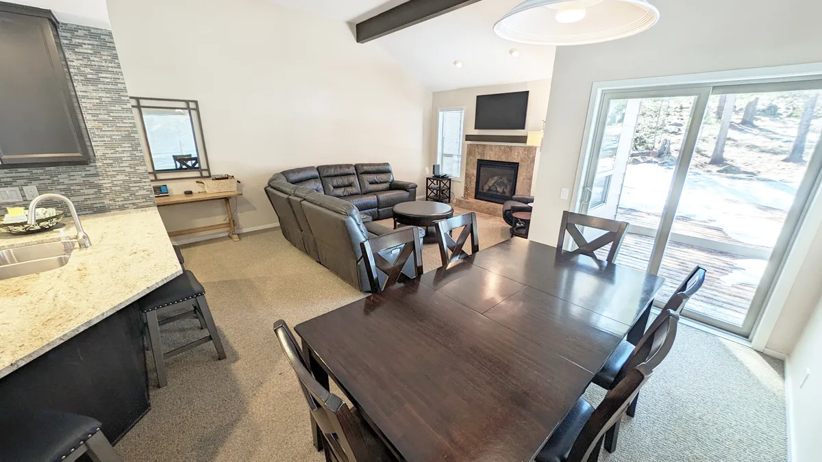 A cozy dining and living space with a fireplace, sofa, dining table, and a sliding glass door that offers a glimpse of the outdoors. The sliding door hints at easy access to trails and outdoor fun.