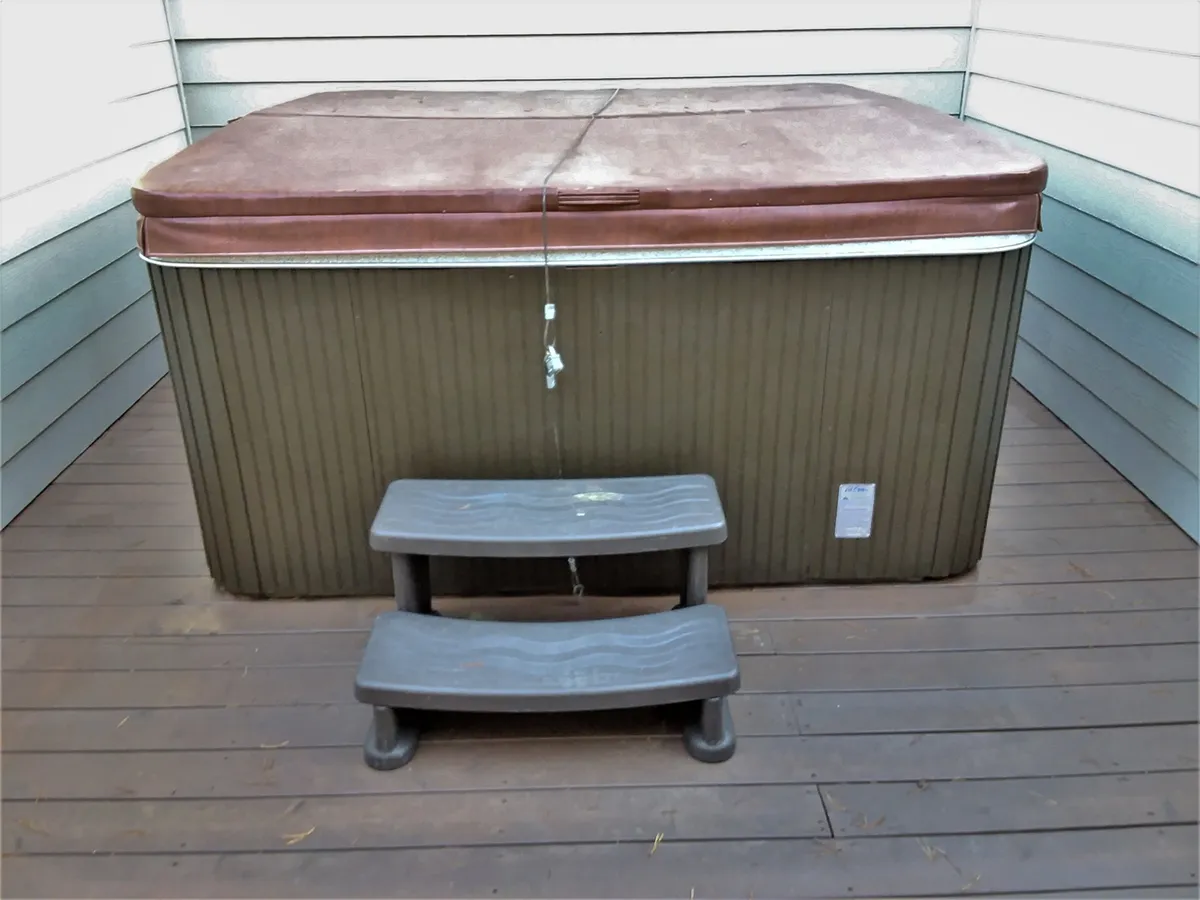 This exterior photo centers on a bubbling hot tub set on a wooden deck, with broad steps leading up to it. Surrounded by trees, the space feels secluded and tranquil, ideal for relaxation or stargazing after an active day.
