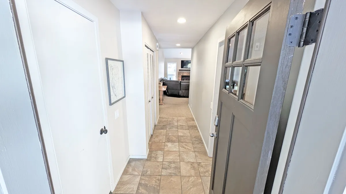 This image features the front door and hallway leading into the main living area, with a framed map on the wall and tile flooring. The view creates a sense of arrival and transition from outside adventures to the welcoming interior.
