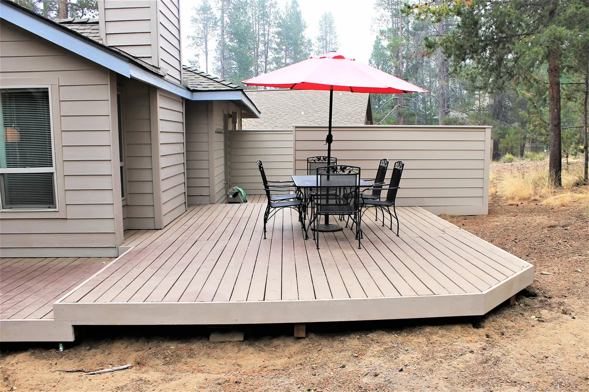 This image captures an inviting deck area with a red umbrella shading an outdoor dining table, surrounded by greenery. The outdoor setting is perfect for family gatherings and socializing after an active day at the SHARC center or local amenities.
